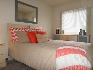 A bed with a mirror above the headboard and dresser below the window