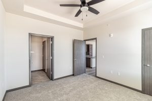 an empty apartment bedroom with ceiling fan and closet doors